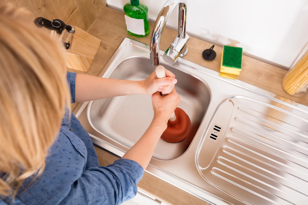 A woman using a plunger in her sink